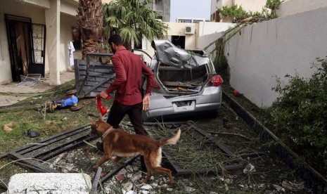   Seorang petugas keamanan menggunakan anjing pelacak memeriksa  lokasi ledakan sebuah bom mobil yang menargetkan Kedubes Perancis di Tripoli, Libya, Selasa (23/4).      (AP/Abdul Majeed Forjani)