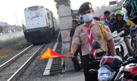  Seorang petugas pramuka memberhentikan pengendara saat ingin melintasi rel kereta api di jalur pantura, Pejagan, Jateng