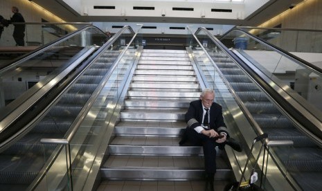   Seorang pilot duduk di depan area keamanan TSA setelah insiden penembakan di Bandara Los Angeles (LAX), California,Jumat (1/11) waktu setempat.  (REUTERS/Lucy Nicholson)