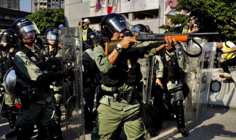 Seorang polisi mengacungkan senjata pengendali kerumunan ke arah demonstran di Hong Kong.