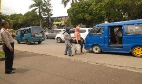 Seorang polisi mengawasi dua penumpang wanita menaiki angkot di depan Mapolresta Depok, Jawa Barat, Jumat (16/12).