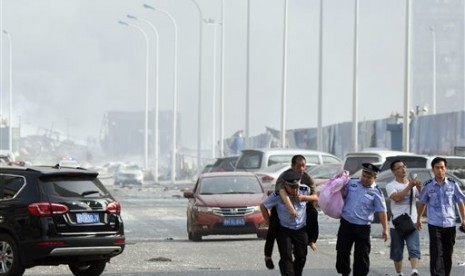 Seorang polisi menggendong warga ke tempat aman di lokasi ledakan di kota pelabuhan Tianjin, Cina, Rabu (12/8).