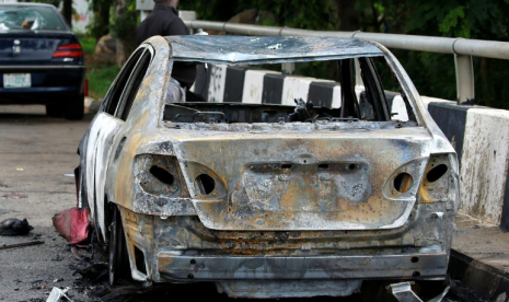  Seorang pria berdiri di dekat bangkai mobil yang terbakar di dekat gedung Parlemen Nigeria usai terjadinya bentrok antara aparat kepolisian dan kelompok demonstran di Abuja, Nigeria, 9 Juli 2019