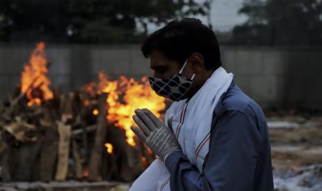 Seorang pria berdoa di depan tumpukan kayu pemakaman kerabatnya, yang meninggal karena COVID-19, di sebuah krematorium di New Delhi, India, Senin, 17 Mei 2021.