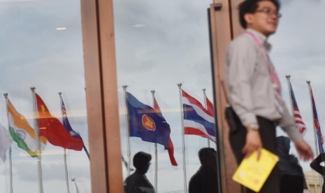 Seorang pria berjalan di depan kaca yang merefleksikan deretan bendera negara peserta Asean Summit ke-28 dan 29 serta Related Summit di National Convention Center, Vientiane, Laos, Minggu (4/9). 