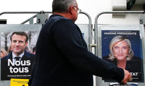 Seorang pria berjalan melewati poster kampanye presiden dari Presiden Prancis dan kandidat tengah untuk pemilihan kembali Emmanuel Macron dan kandidat presiden sayap kanan Prancis Marine Le Pen di Anglet, barat daya Prancis, Rabu, 8 April 2022. Pilpres di Prancis menawarkan Macron dan Le Pen yang dinilai bersikap anti-Muslim.