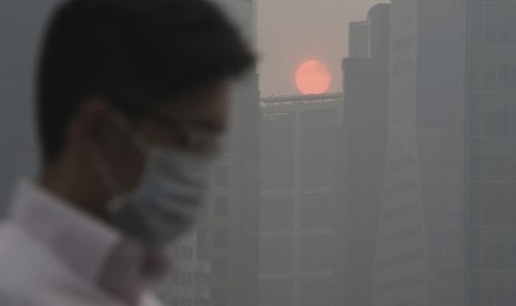 Seorang pria mengenakan masker berjalan saat matahari terbenam di antara bangunan yang tertutup kabut di kawasan pusat bisnis Singapura,Kamis (20/6).    (AP/Joseph Nair)