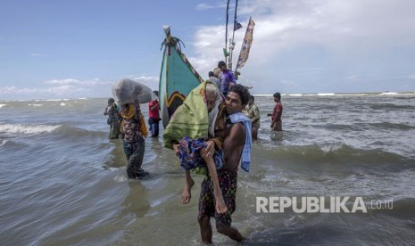 Seorang pria Muslim Rohingya berjalan ke pantai yang membawa seorang wanita tua setelah mereka tiba di sebuah kapal dari Myanmar ke Bangladesh di Shah Porir Dwip, Bangladesh, Kamis, (14/9).