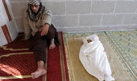  Seorang pria Palestina duduk di samping jenazah anaknya yang berusia satu setengah tahun di Kamp Pengungsi Bureij,Gaza, Ahada (18/11). (AP Photo/Adel Hana)