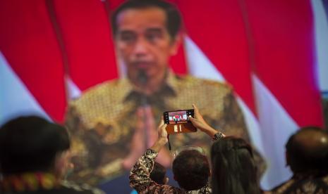 Seorang tamu undangan merekam Presiden Joko Widodo saat berpidato secara virtual dalam acara puncak Hari Pers Nasional (HPN) 2021 di Ancol, Jakarta, Selasa (9/2/2021). Presiden dalam pidatonya selain mengapresiasi peran insan pers yang membantu pemerintah mengedukasi penerapan protokol kesehatan juga mengatakan pemerintah membebaskan pajak penghasilan karyawan bagi wartawan untuk meringankan beban insan pers Indonesia di tengah menghadapi masa sulit akibat pandemi COVID-19.