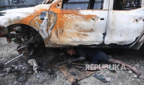 Seorang teknisi berusaha melepas onderdil yang masih bisa digunakan dari mobil yang hangus terbakar pasca unjuk rasa yang berujung anarkis di Jalan Trans Papua Pikhe, Wamena, Kabupaten Jayawijaya, Papua, Rabu (9/10/2019). 