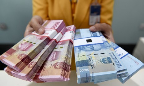 Seorang teller Bank Mandiri menunjukkan uang pecahan Rp100.000 dan Rp50.000 di Plasa Mandiri, Jakarta, Senin (8/7/2019).