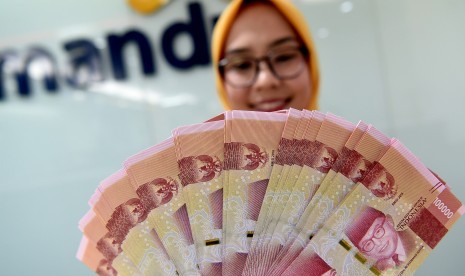 Seorang teller Bank Mandiri menunjukkan uang pecahan Rp100.000 di Plasa Mandiri, Jakarta, Senin (8/7/2019).