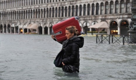 Seorang turis dengan mengangkat koper besar miliknya melintas di St Mark's Square, Venice, Italia, yang direndam banjir, Ahad (11/11). 