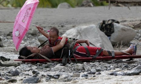   Seorang wanita hamil yang selamat dari banjir memegang anaknya diatas tandu sambil menunggu untuk dievakuasi di kota New Bataan,Filipina, Kamis (6/12). (Reuters/Erik De Castro)