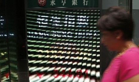 Seorang wanita melintas di depan papan elektronik yang menunjukan indeks saham Hong Kong