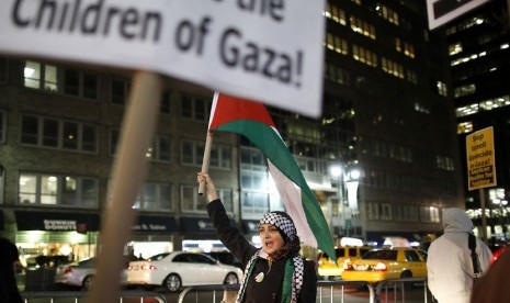 Seorang wanita membawa bendera Palestina saat melakukan aksi protes di seberang kantor konsulat Israel di New York, Jumat (16/11). (Reuters/Carlo Allegri)