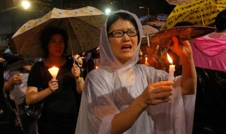 Seorang wanita memegang lilin di bawah hujan deras saat puluhan ribu orang menghadiri upacara lilin di Victoria Park, Hong Kong, Selasa (4/6). 