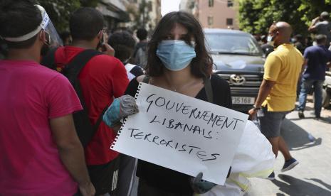 Seorang wanita memegang plakat dalam bahasa Prancis yang bertuliskan, Teroris pemerintah Lebanon, di samping konvoi Presiden Prancis Emmanuel Macron saat dia mengunjungi lingkungan Gemayzeh, yang mengalami kerusakan parah akibat ledakan pada hari Selasa yang menghantam pelabuhan Beirut, Lebanon, Kamis, 6 Agustus 2020.