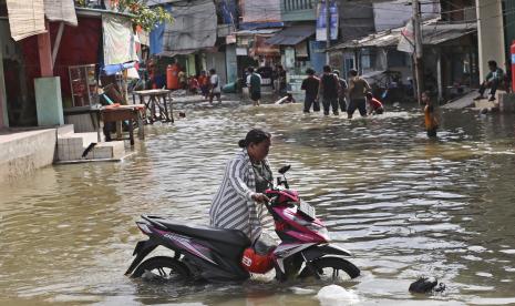 Seorang perempuan mendorong sepeda motornya melewati air saat banjir rob di Muara Baru, Jakarta Utara, pada Selasa, 9 November 2021. 