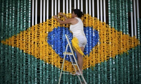 Seorang wanita mengikati pita membentuk pola bendera nasional Brasil di jalanan yang dihiasi warga setempat untuk menyambut Piala Dunia 2014. 