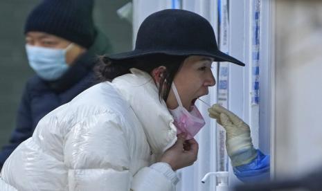  Seorang wanita menjalani swab tenggorokan COVID-19 secara rutin di tempat pengujian virus corona di Beijing, Ahad, 4 Desember 2022. China pada Minggu melaporkan dua kematian tambahan akibat COVID-19 karena beberapa kota bergerak dengan hati-hati untuk melonggarkan pembatasan anti-pandemi di tengah meningkatnya frustrasi publik yang vokal atas tindakan tersebut.