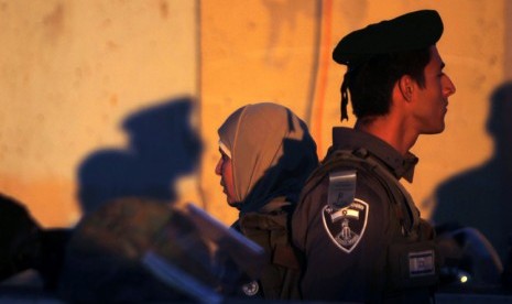 Seorang wanita Palestina berdiri di belakang polisi Israel saat melintasi pos pemeriksaan Qalandiya di Tepi Barat Ramallah, Jumat (10/8).  (Mohamad Torokman/Reuters)