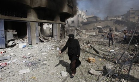 Seorang wanita Palestina berjalan di depan puing bangunan yang hancur akibat serangan udara Israel di Kota Gaza, Ahad (18/11).