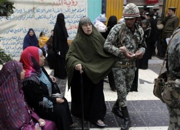 Seorang wanita warga Mesir dibimbing oleh anggota militer menuju tempat pemungutan suara pemilihan umum parlemen di Qalyobeia, Rabu (4/1).