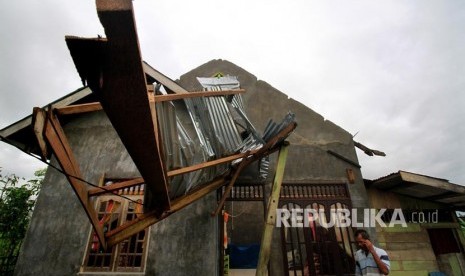 Seorang warga berada di depan rumah yang mengalami kerusakan pada bagian atap akibat diterjang angin puting beliung (ilustrasi)