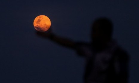 Seorang warga berfoto dengan latar belakang fenomena bulan Supermoon di kota Lhokseumawe, Aceh, Selasa (19/2/2019).(Antara/Rahmad)