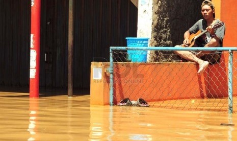   Seorang warga bermain gitar di tengah pemukiman yang terendam banjir di Baleendah Kabupaten Bandung, Senin(3/3).  (foto: Septianjar Muharam)