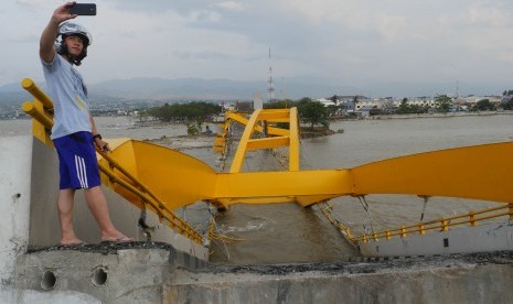 Seorang warga berswafoto dengan latar belakang jembatan Ponulele yang ambruk di pantai Talise, Palu Sulawesi Tengah, Selasa (16/10). Jembatan merupakan salah satu aset milik negara.