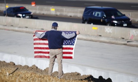 Seorang warga Colorado, Amerika Serikat (AS) membentangkan bendera AS saat kendaraan yang membawa jenazah anggota polisi korban penembakan melintas, Ahad (31/12).