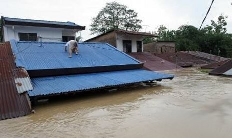 Seorang warga di Mandailing Natal, Sumatra Utara, naik ke atap rumahnya saat banjir melanda tahun lalu.