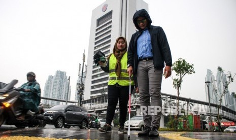 Seorang warga (kanan) merasakan menjadi penyandang disabilitas pada acara Kota untuk Semua di trotoar Jalan Sudirman, Jakarta, Senin (3/12/2018). 