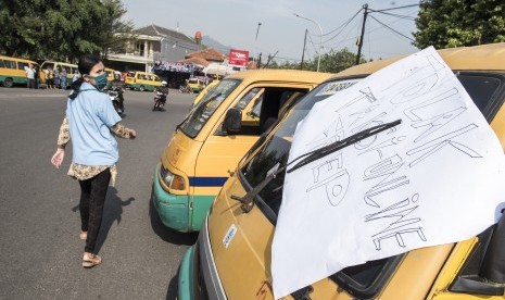 Seorang warga melintas di depan angkutan umum saat unjuk rasa sopir angkutan umum dari empat trayek di Bundaran Leuwigajah, Cimahi Selatan, Kota Cimahi, Jawa Barat, Senin (25/9). 