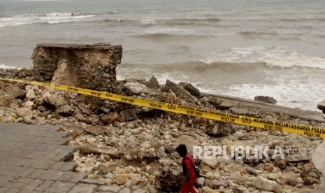 Seorang warga melintas di dermaga tempat wisata kuliner yang rusak akibat diterjang gelombang tinggi di pesisir pantai Kota Kupang, NTT beberapa waktu lalu 