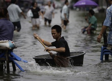 Seorang warga melintasi jalan di kota Bangkok dengan menggunakan wadah serta sapu sebagai dayung, Jumat, 28/10. (AP)