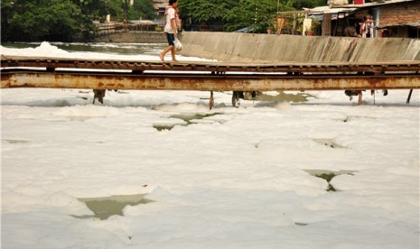 Seorang warga melintasi jembatan kayu di atas sungai yang tercemar. (ilustrasi) 