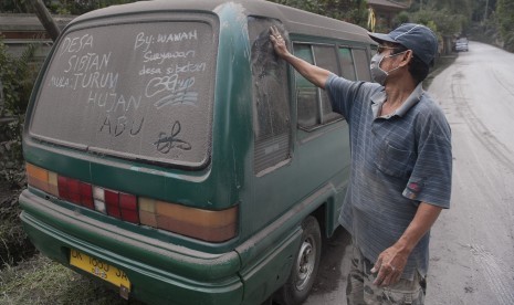 Seorang warga membersihkan mobilnya dari abu letusan Gunung Agung, di Desa Sebetan, Karangasem, Bali, Ahad (26/11).