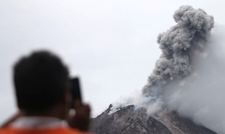 Seorang warga memotret Gunung Sinabung mengeluarkan material vulkanis ketika erupsi, tampak dari Desa Tiga Serangkai, Karo, Sumatera Utara, Jumat (13/11).