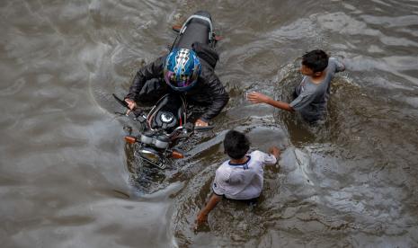 Seorang warga mendorong motornya yang mogok karena nekat menembus banjir yang merendam Jalur Pantura Kaligawe-Genuk, Semarang, Jawa Tengah, Rabu (24/2).