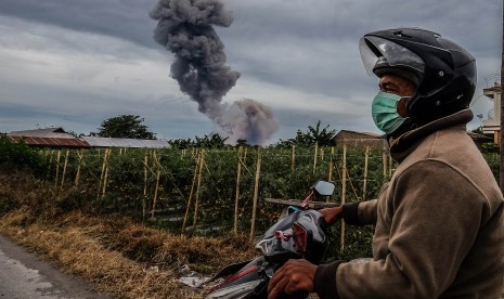 Seorang warga mengendarai sepeda motor ketika Gunung Sinabung mengeluarkan material vulkanik, di Desa Raja Payung, Karo, Sumatera Utara, Kamis (26/5).