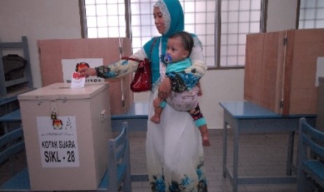  Seorang warga menggendong anaknya menyalurkan suaranya di Pilpres 2014 di Sekolah Indonesia Kuala Lumpur, Malaysia, Sabtu (5/7).