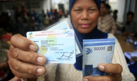 Seorang warga menunjukan kartu dan uang usai mengantre pembagian dana program keluarga harapan (PKH)