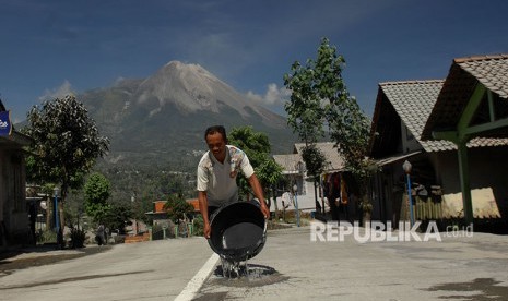 Seorang warga menyiram jalan raya yang tertutup abu vulkanis Gunung Merapi di Wonolelo, Sawangan, Magelang, Jawa Tengah, Jumat (1/6).