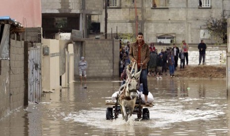 Seorang warga Palestina dengan menaiki gerobak yang ditarik seekor keledai melintasi jalan yang banjir akibat hujan lebat di Rafah,  selatan Jalur Gaza, Rabu (9/1). (Reuters/Ibraheem Abu Mustafa)