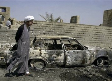 Seorang warga Syiah melintas di sebuah rongsokan bom mobil yang diledakkan di Baghdad, Irak.