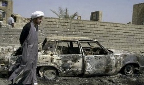 Seorang warga Syiah melintas di sebuah rongsokan bom mobil yang diledakkan di Baghdad, Irak.